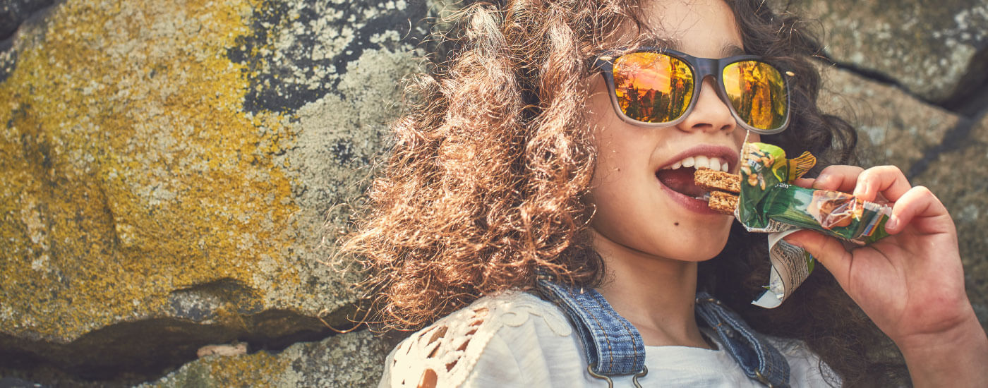 A curly hair wearing glares smiling while eating granola bar